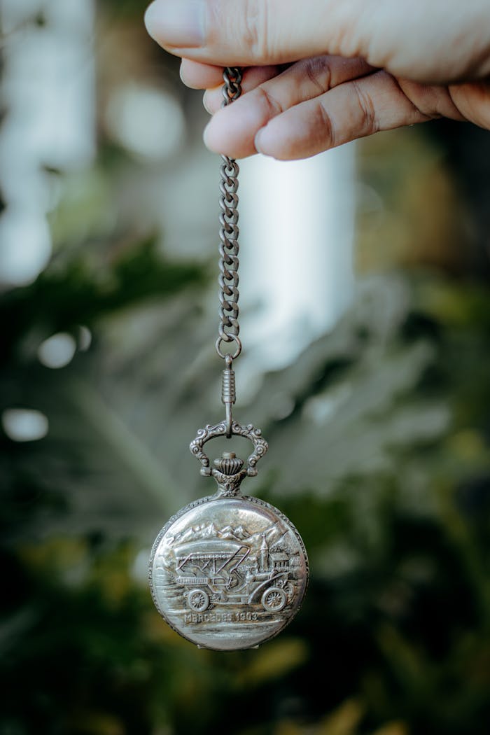 Close-up of a vintage pocket watch held by a hand against a blurred natural background.
